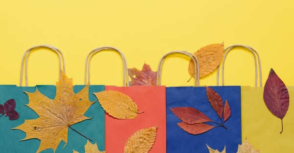 Green, Red, and Blue Shopping Bags Over a Yellow Background With Autumn Leaves